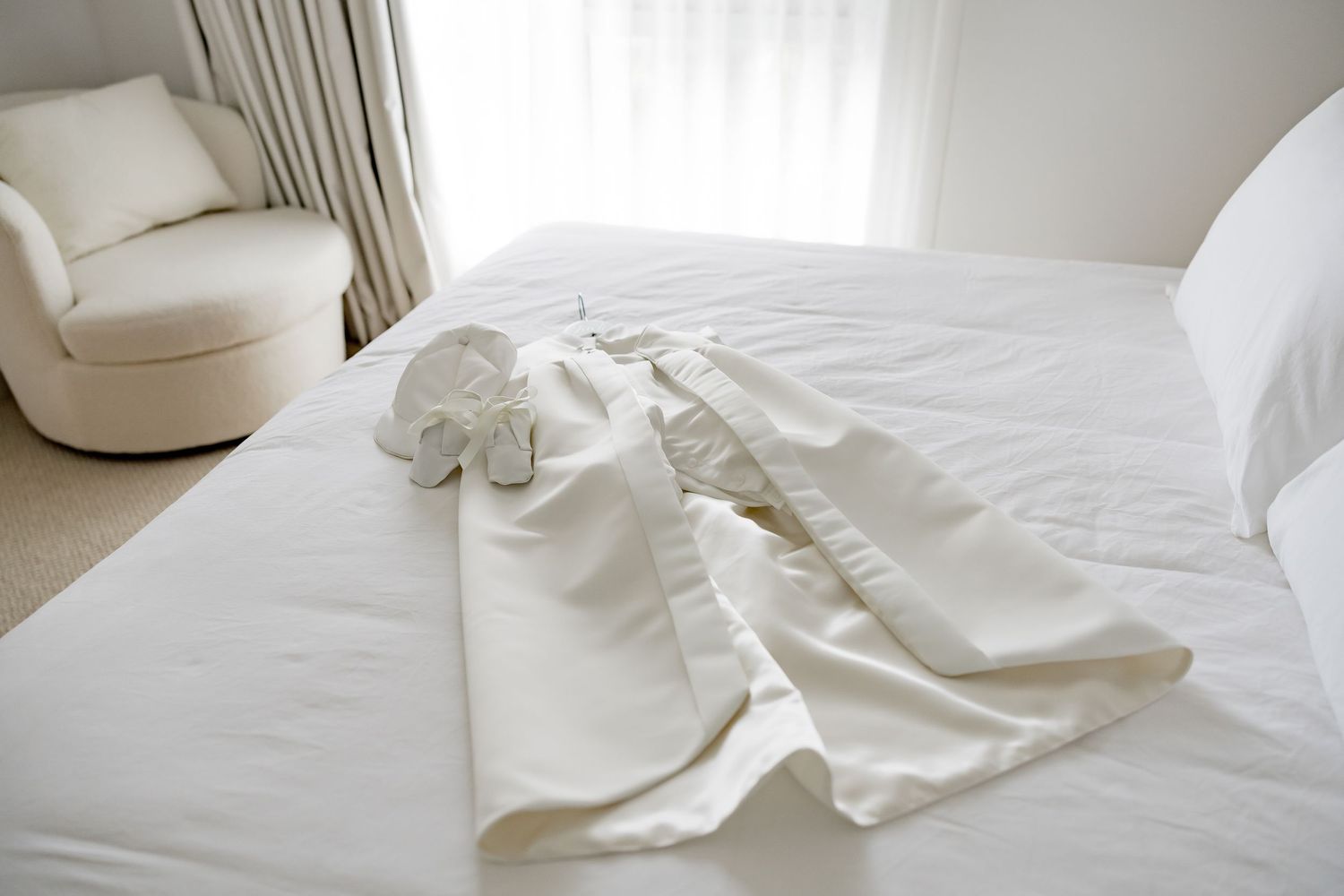 A white dress shirt laid out neatly on a white hotel bed with a cream colored armchair in the background.