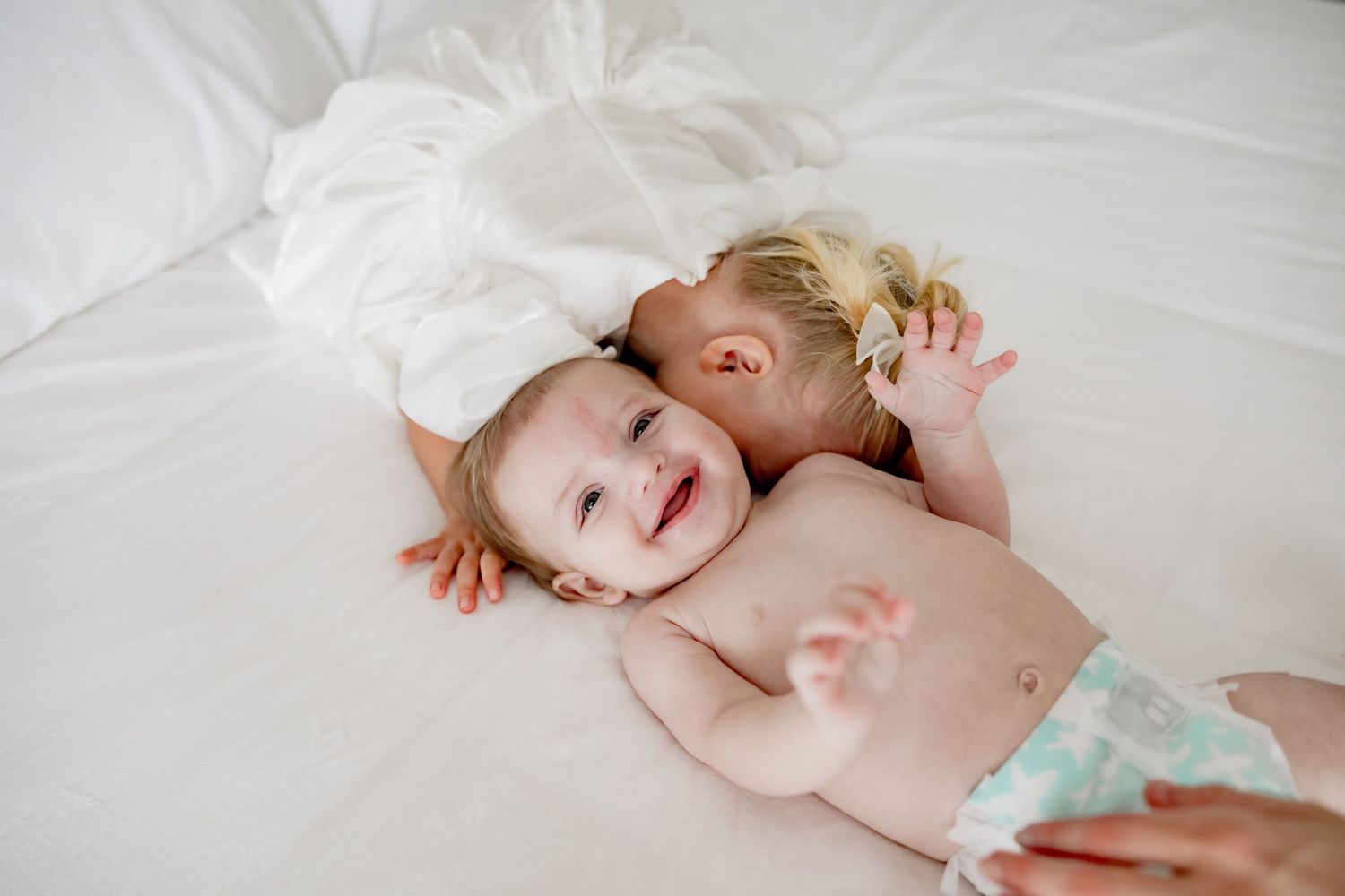Baby lying on white bedding smiling at camera in progressive stages.