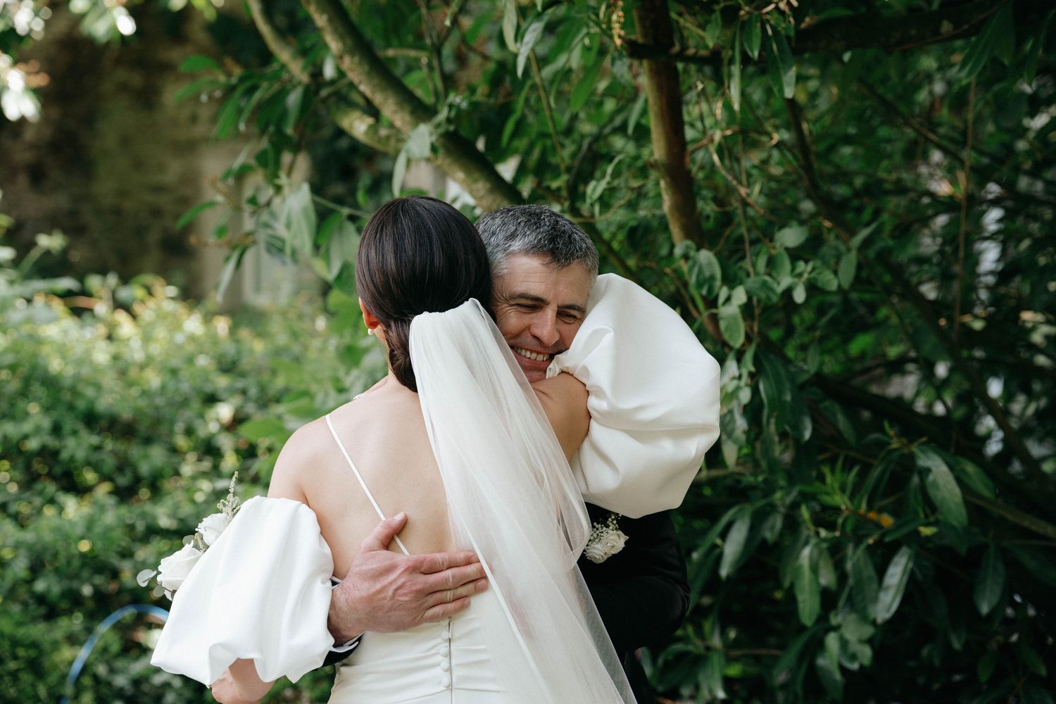 Two people embrace outdoors in a garden setting wearing white clothing, creating an intimate moment among the greenery. Top wedding photos
