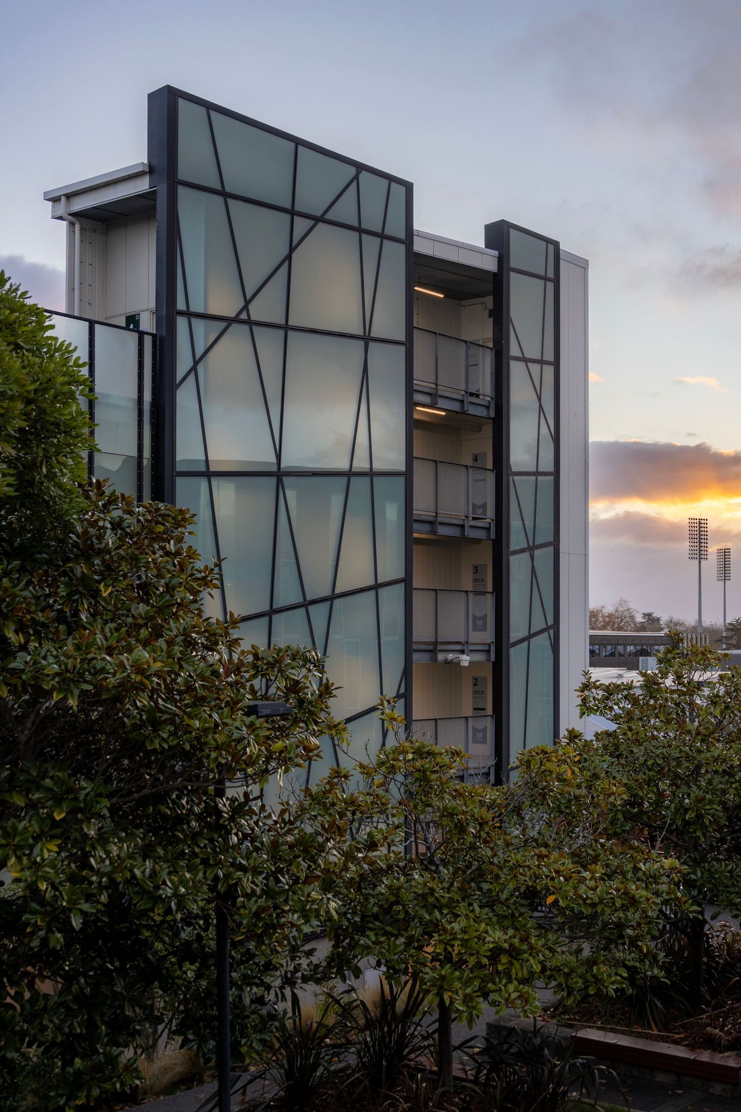 Angled glass apartment façade with frosted panels and steel supports at sunset.