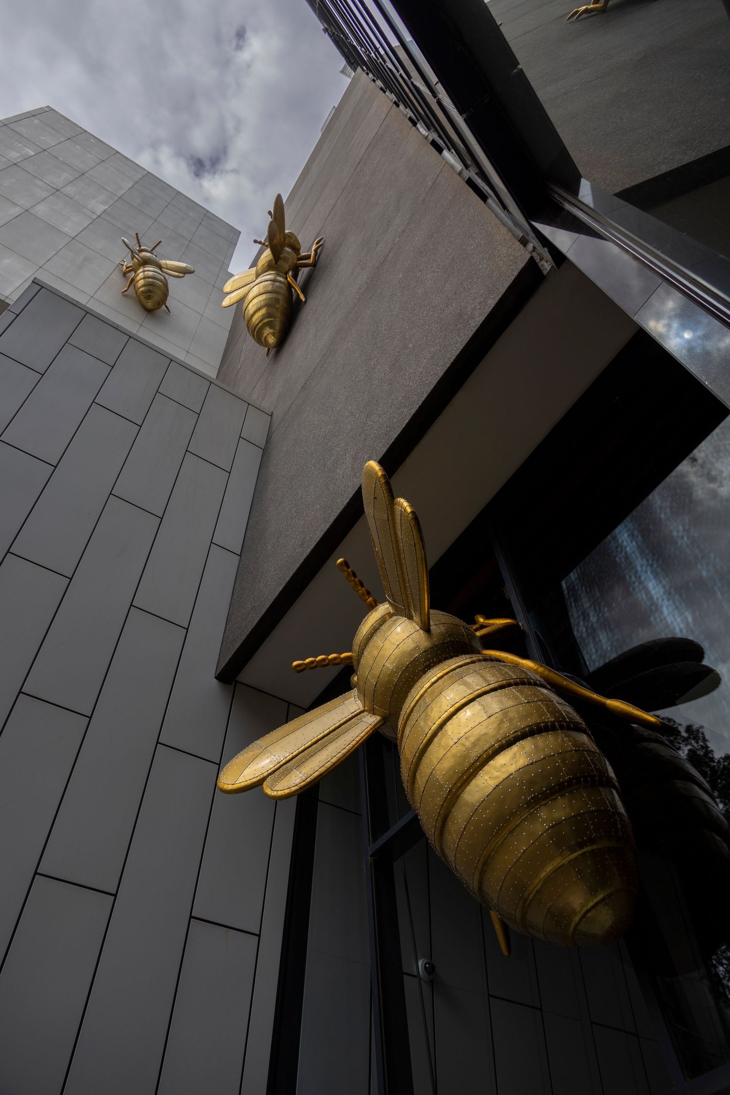 Sculptural golden bees climbing the side of a sleek grey high-rise building.