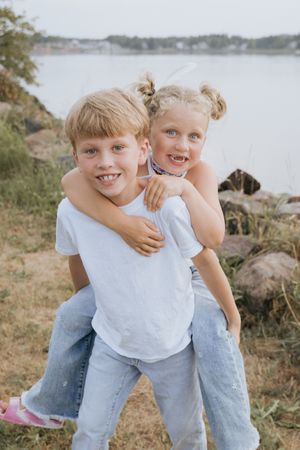 Siblings piggy back ride in candid moment photography at Shediac Wharf, Moncton family photography packages, child photographer in Canada