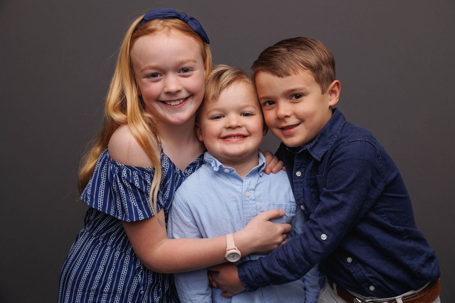 A collection of six photographs showing children hugging and posing together against a dark gray backdrop.