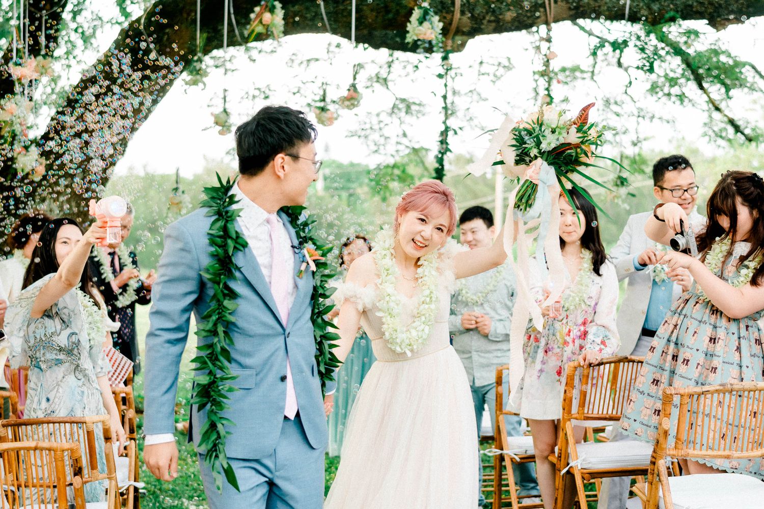Joyful ceremony exit celebration at an outdoor garden wedding ceremony with bamboo chairs and tropical floral decorations.