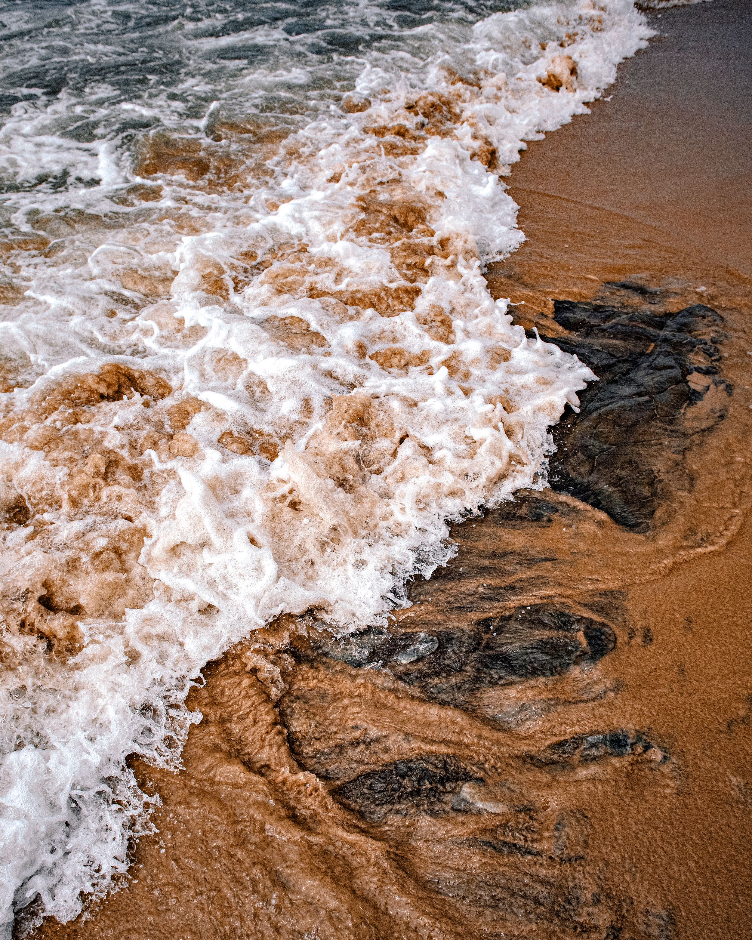 Foamy brown ocean waves washing over dark wet sand on a beach shoreline.