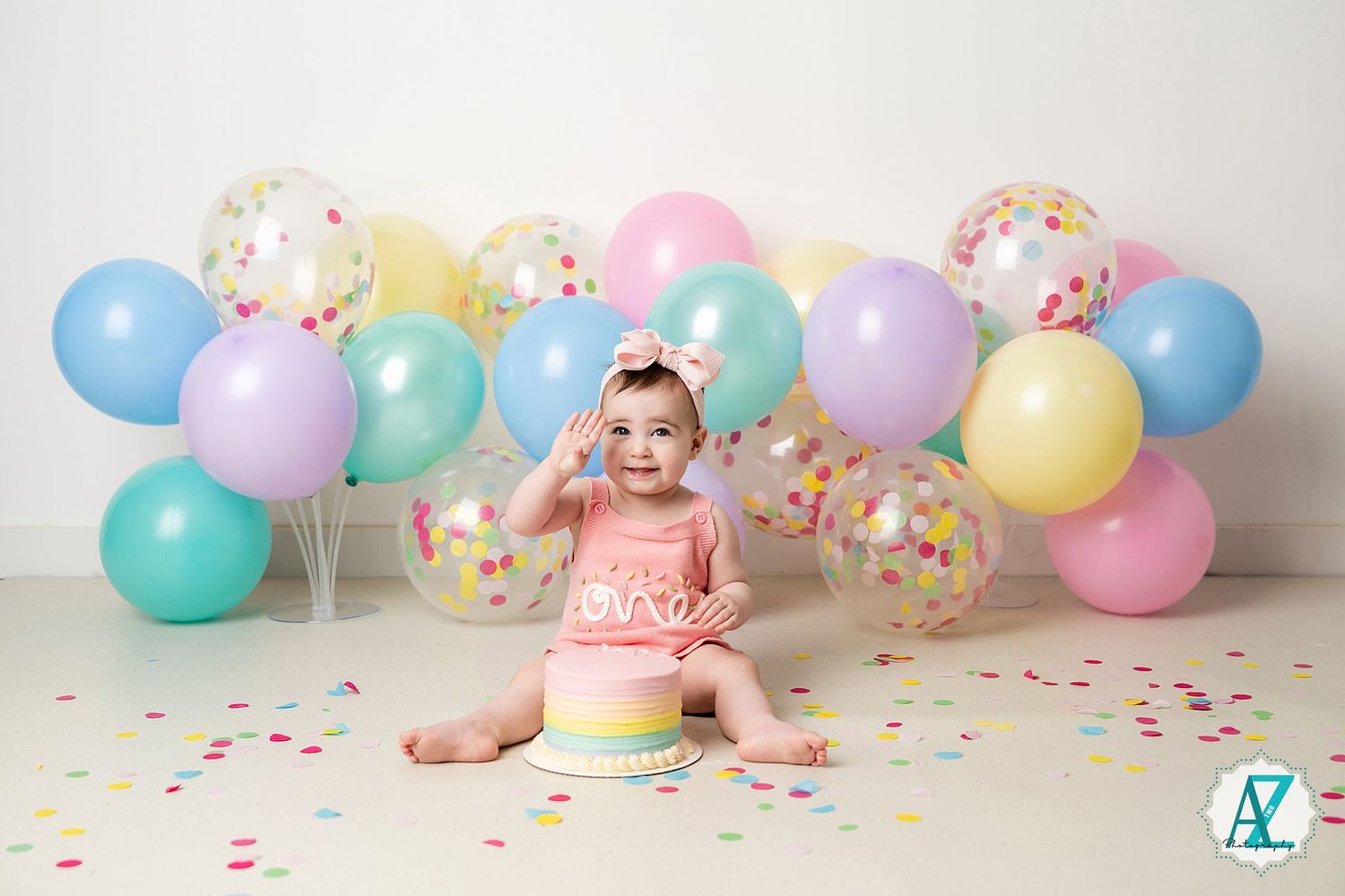 Pastel balloon garland and sprinkle decorations create a festive cake smash setup against a light gray backdrop.