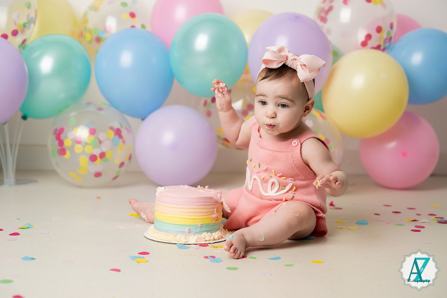 First birthday celebration setup with colorful balloons, confetti and smash cake in pastel colors.