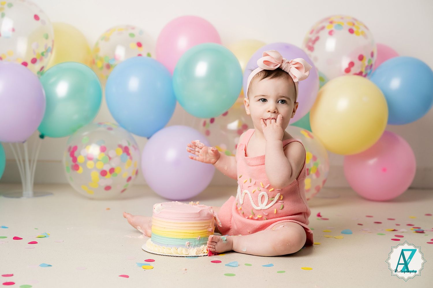 First birthday cake smash photo with pastel balloons and confetti background setup.