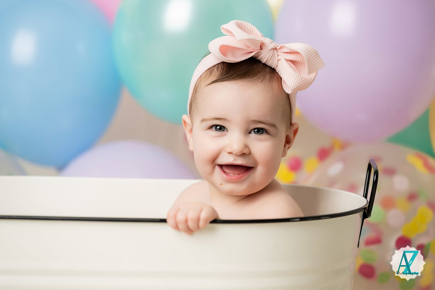 Joyful first birthday photo shoot with pastel balloons and white wooden basin.