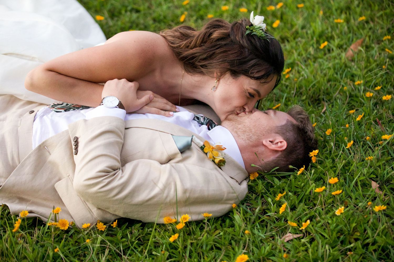 Two people laying in grass surrounded by small yellow wildflowers.