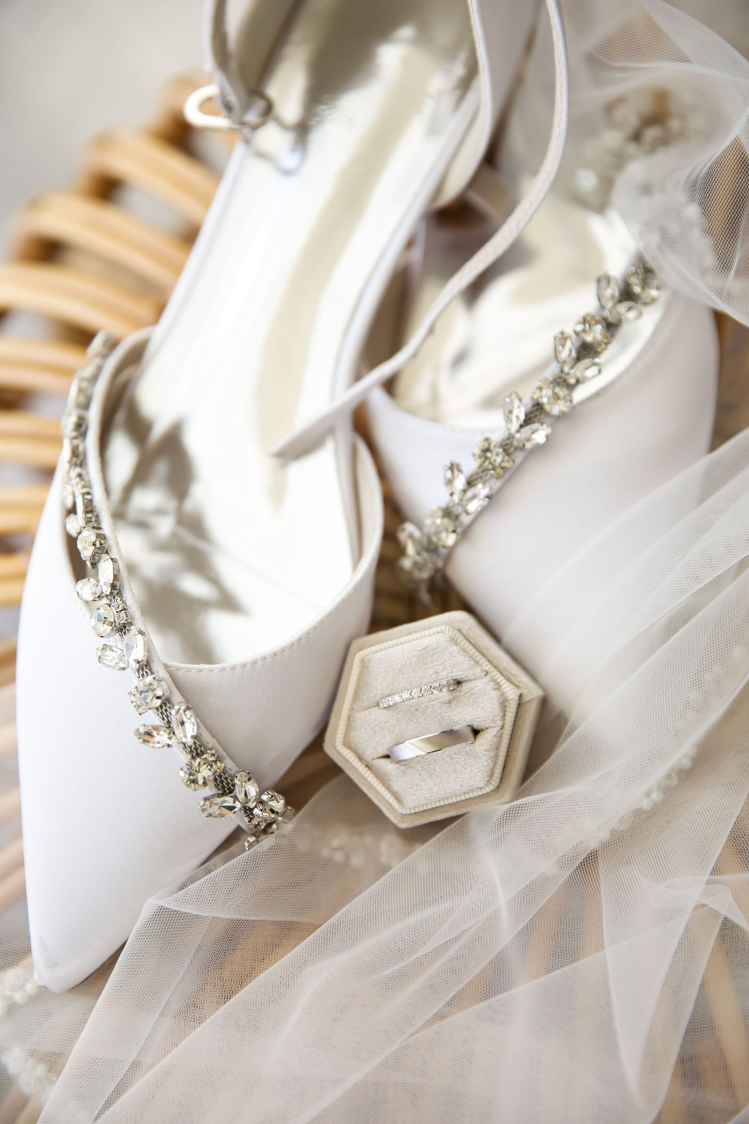 White bridal shoes with crystal embellishments displayed with a hexagonal ring box on delicate tulle fabric.