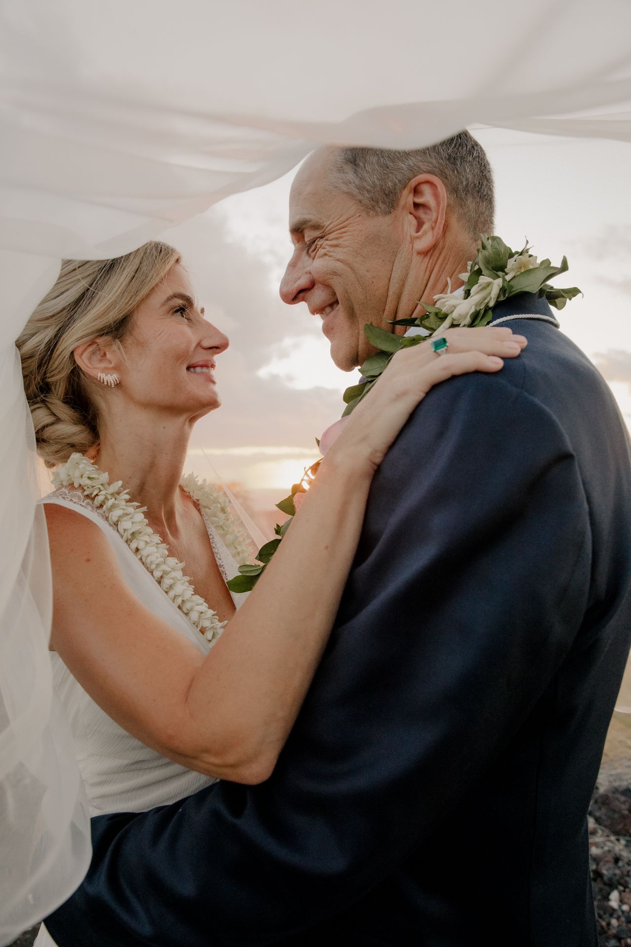 A tender moment shared between a couple wearing traditional Hawaiian leis during what appears to be a wedding ceremony.