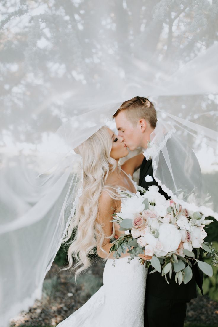 Romantic outdoor wedding portrait captures newlyweds in a soft, ethereal embrace with a blush and white floral bouquet.