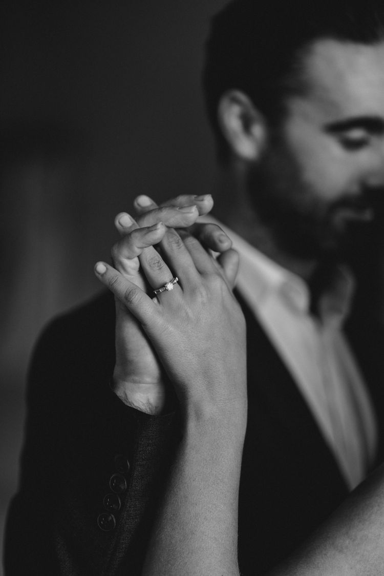 An intimate black and white photograph capturing hands with a wedding ring in a tender moment.