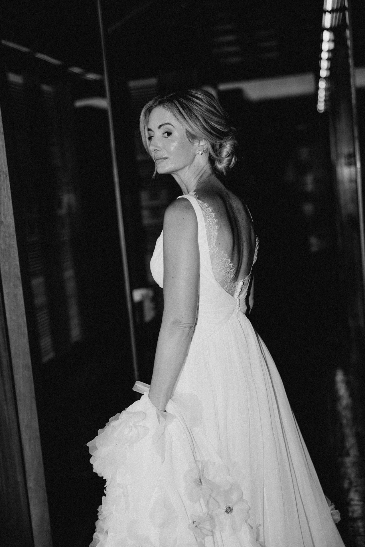 A bride in a flowing white wedding gown and veil poses dramatically in a dark venue with dramatic lighting.