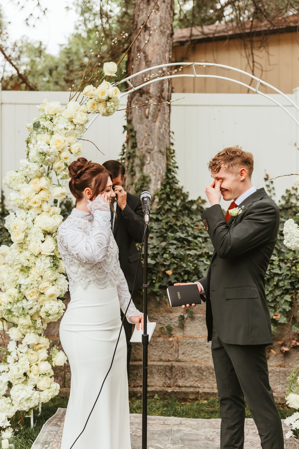 A touching wedding ceremony moment at an outdoor garden venue with floral arch decorations and stone pathway.