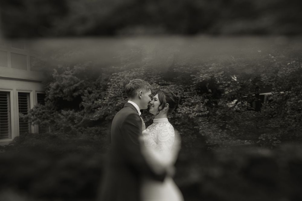 A romantic black and white wedding photograph taken with a dreamy blurred vignette effect in a garden setting.