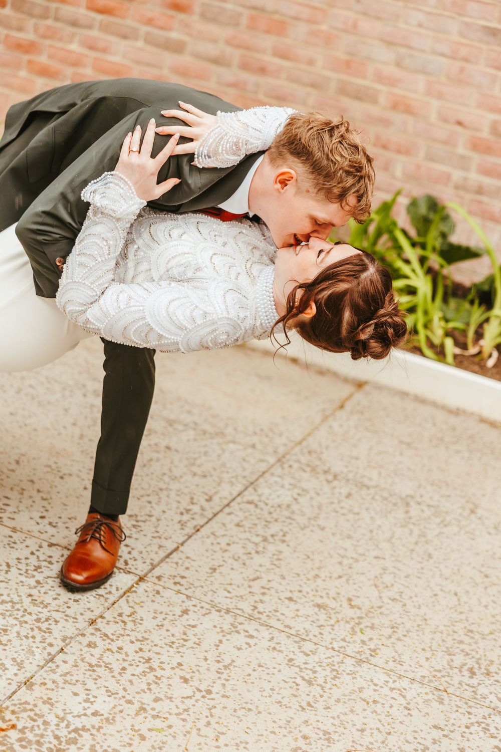Romantic dip kiss between newlyweds showcasing bride's detailed lace dress and groom's brown leather shoes.