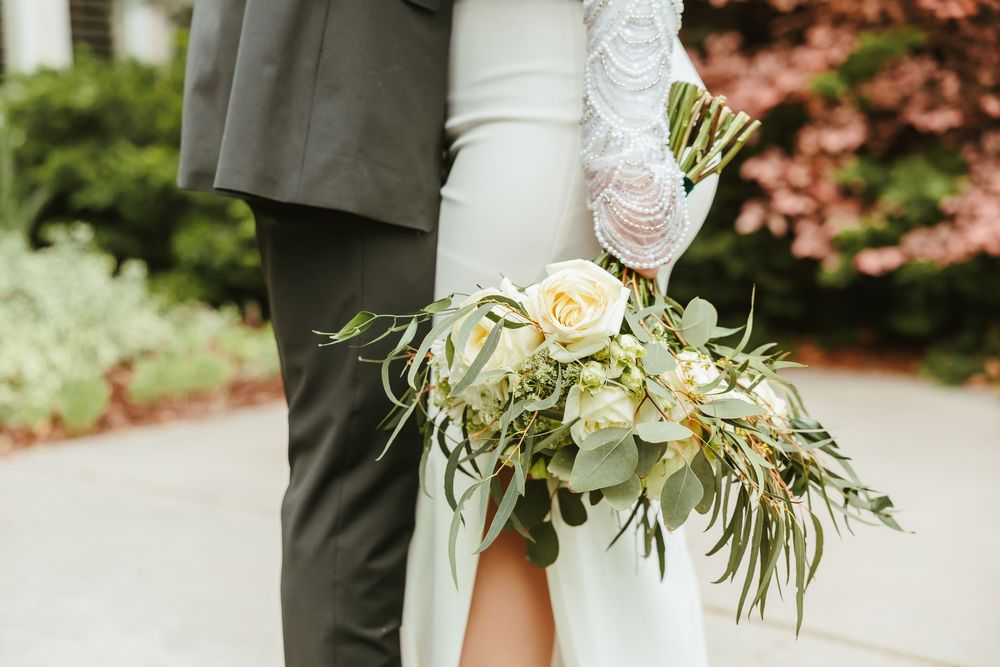 Close up of white and green cascading bridal bouquet against wedding attire.