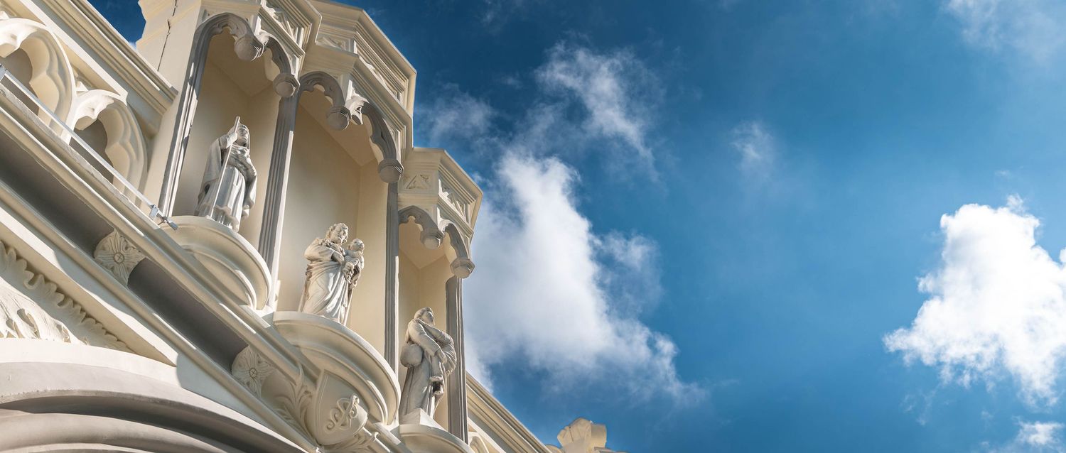 Architectural details of ornate white building facades against a bright blue sky with puffy clouds.
