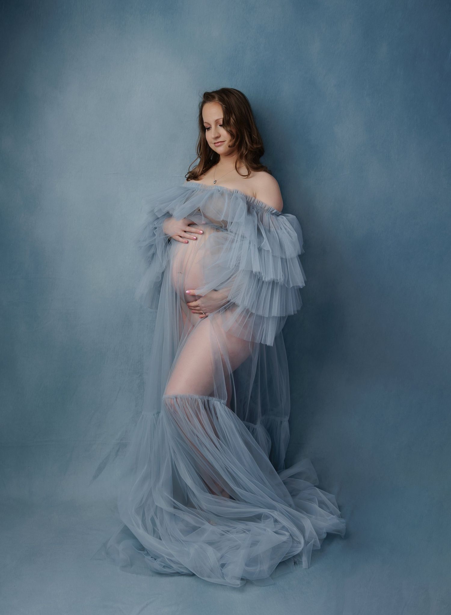 Austin maternity photography studio portrait of expecting mother wearing flowing blue gown against painted backdrop