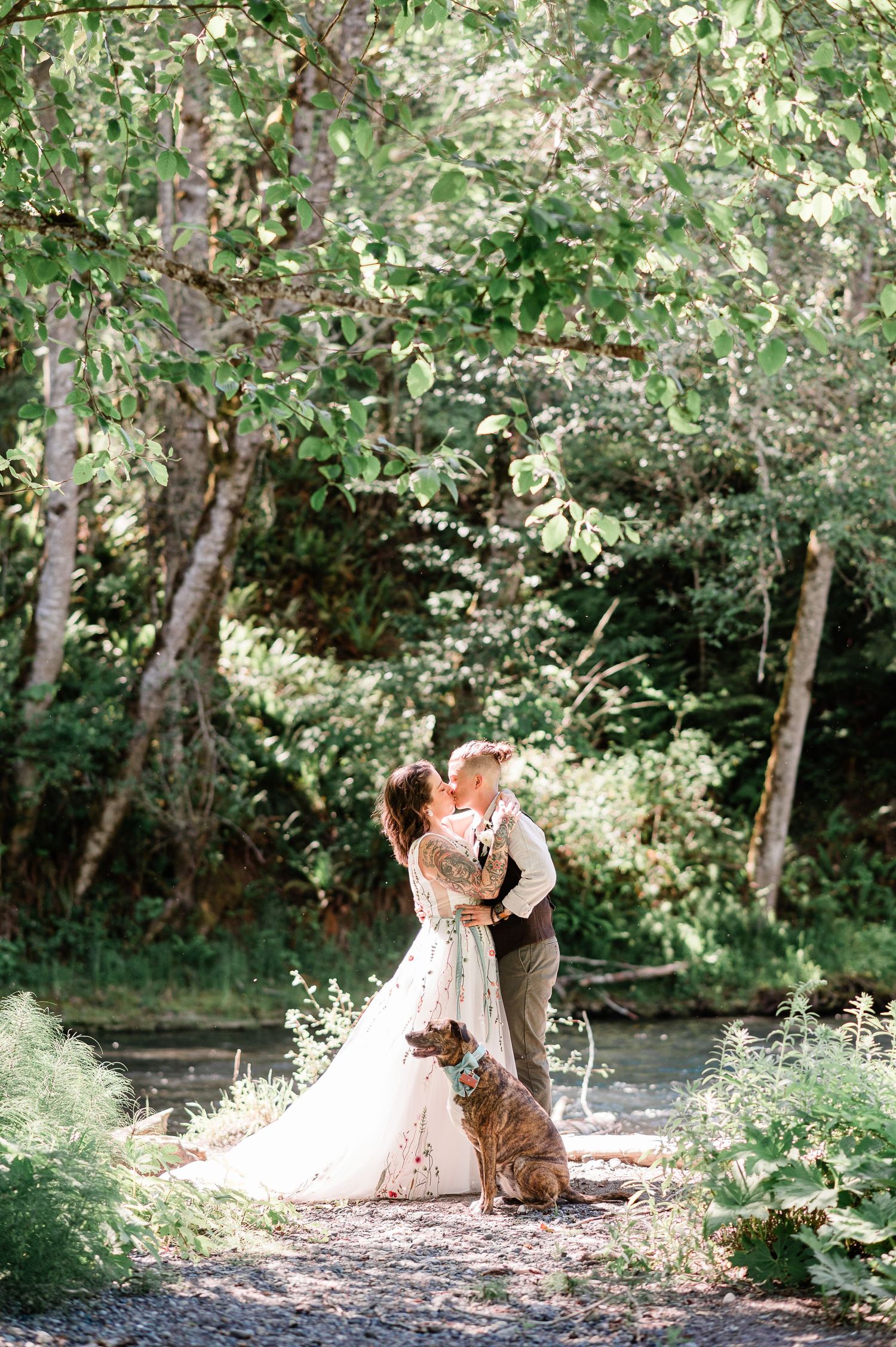 two brides kissing by river with a dog at their feet