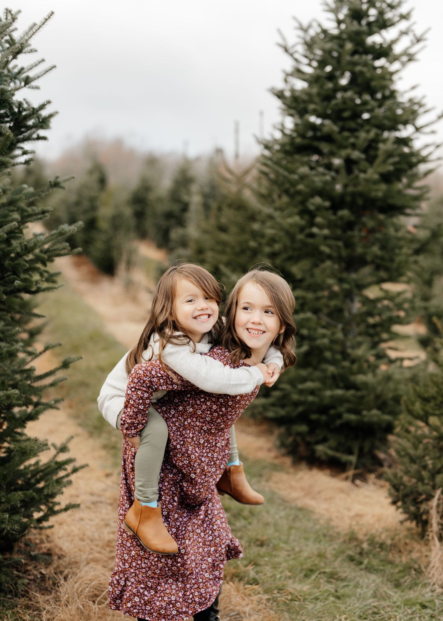 Two children in coordinating floral dresses share playful moment at Christmas tree farm.