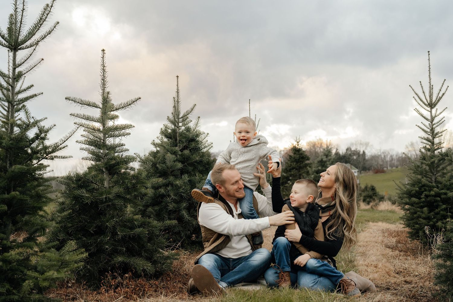 Family shares joyful moment together while sitting among Christmas trees.