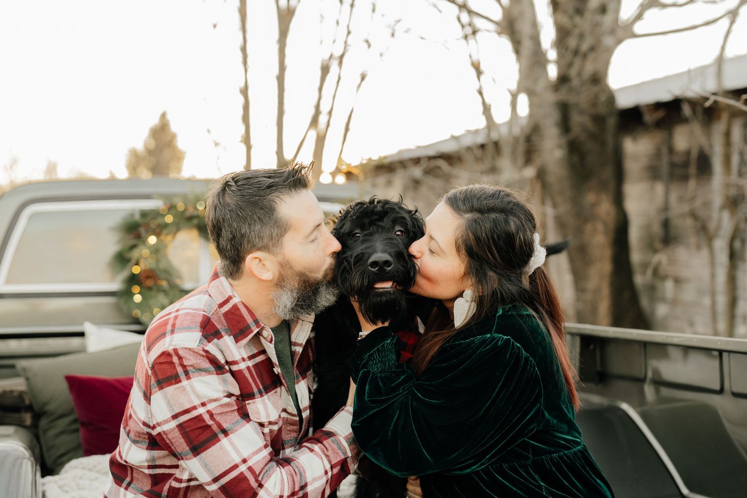 A couple sharing affectionate moment with their black dog in truck bed during winter.
