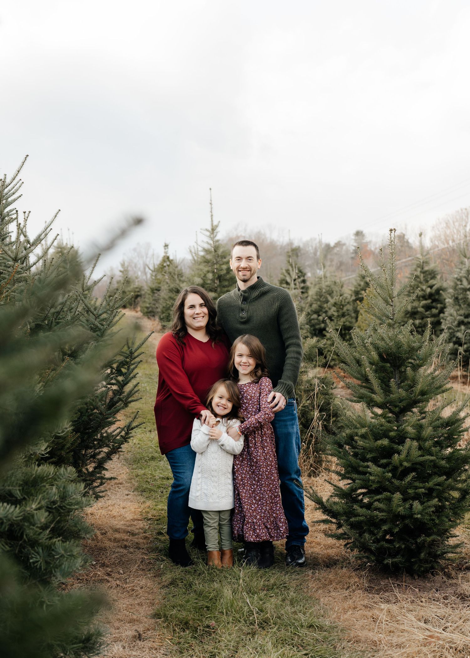 A family portrait among evergreen trees at a Christmas tree farm.