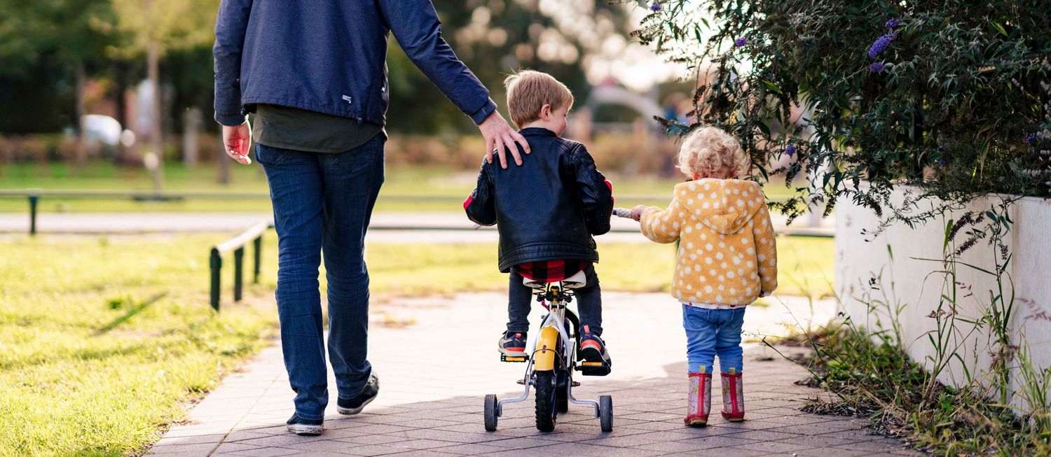 Family walking together on path with toddler on balance bike.
