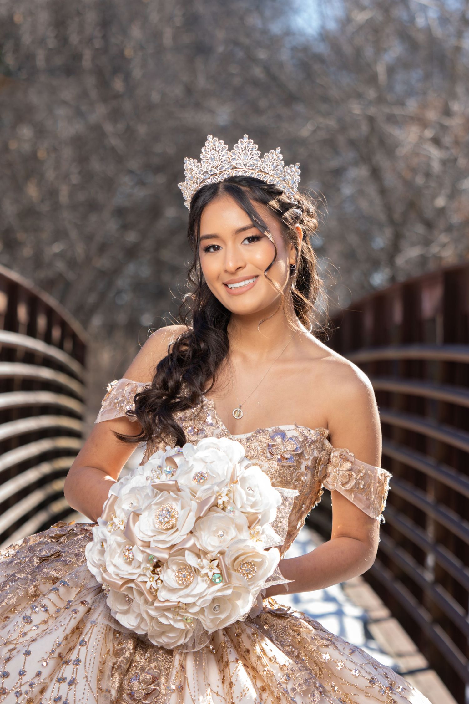 Person in sparkly gold ball gown posing outdoors against evergreen trees.