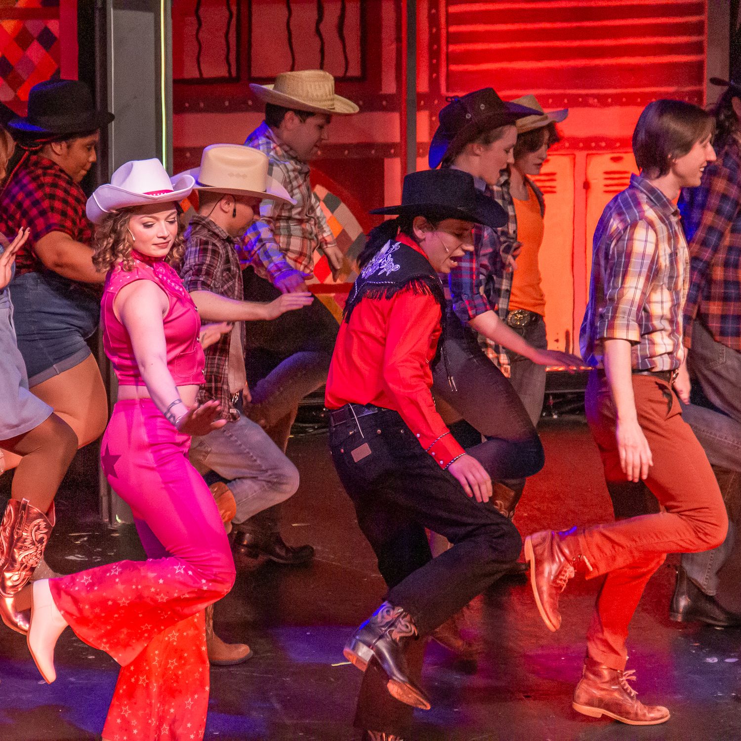 Dancers perform in western attire during a lively country dance number on stage.
