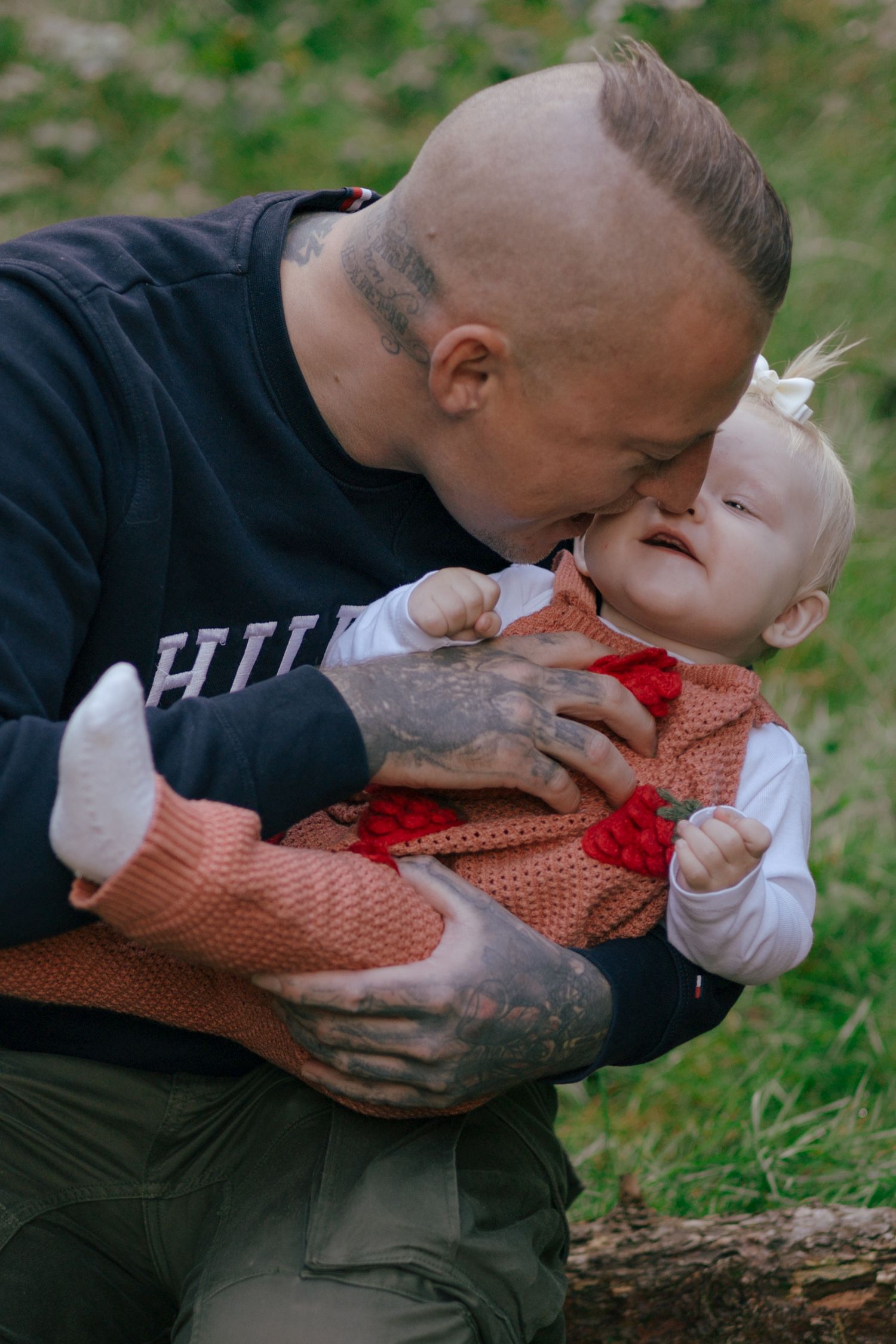 Tender moment shared between adult and baby in orange outfit outdoors.