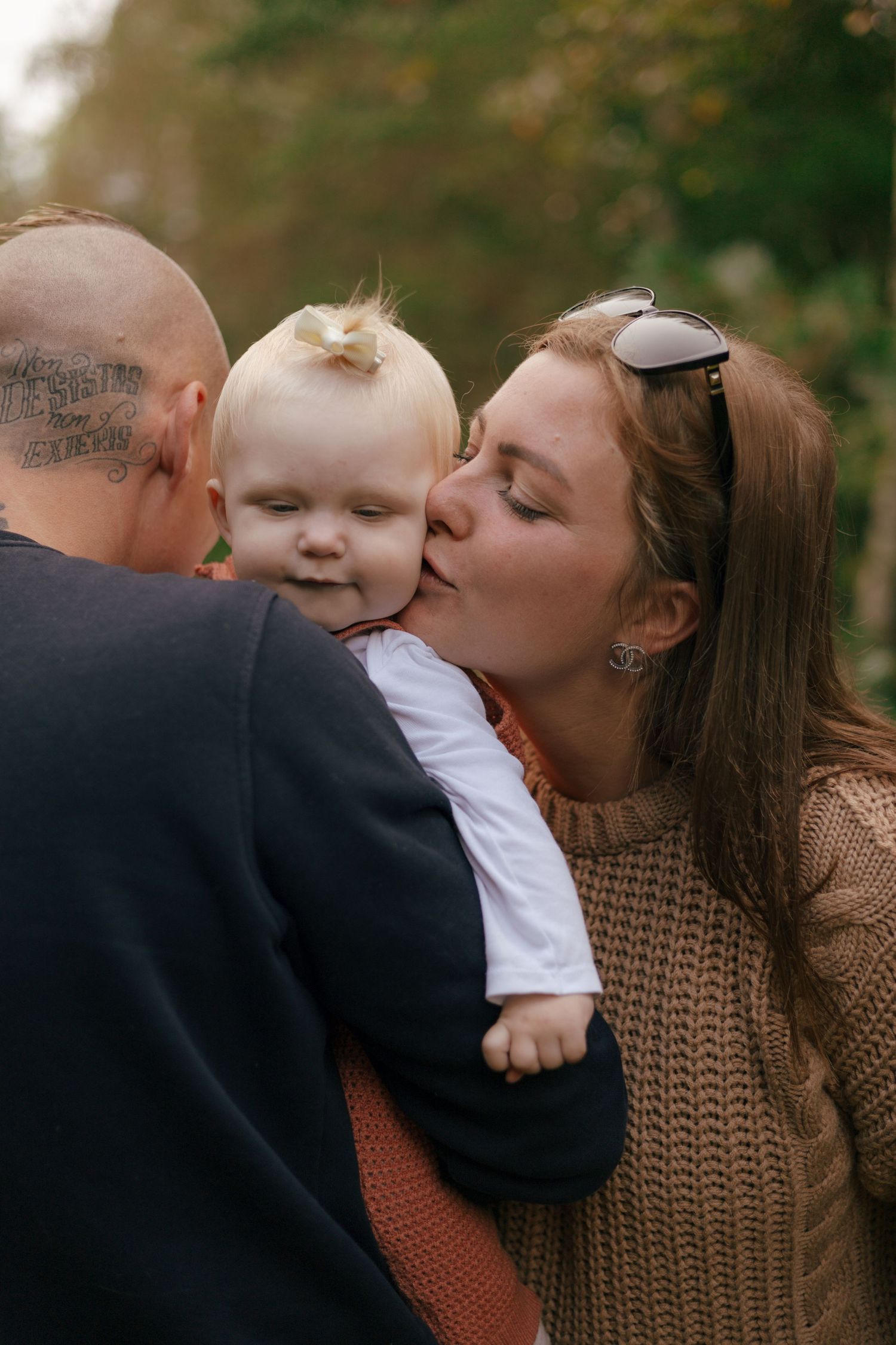 Sweet family moment captured outdoors with baby in white and orange outfit.