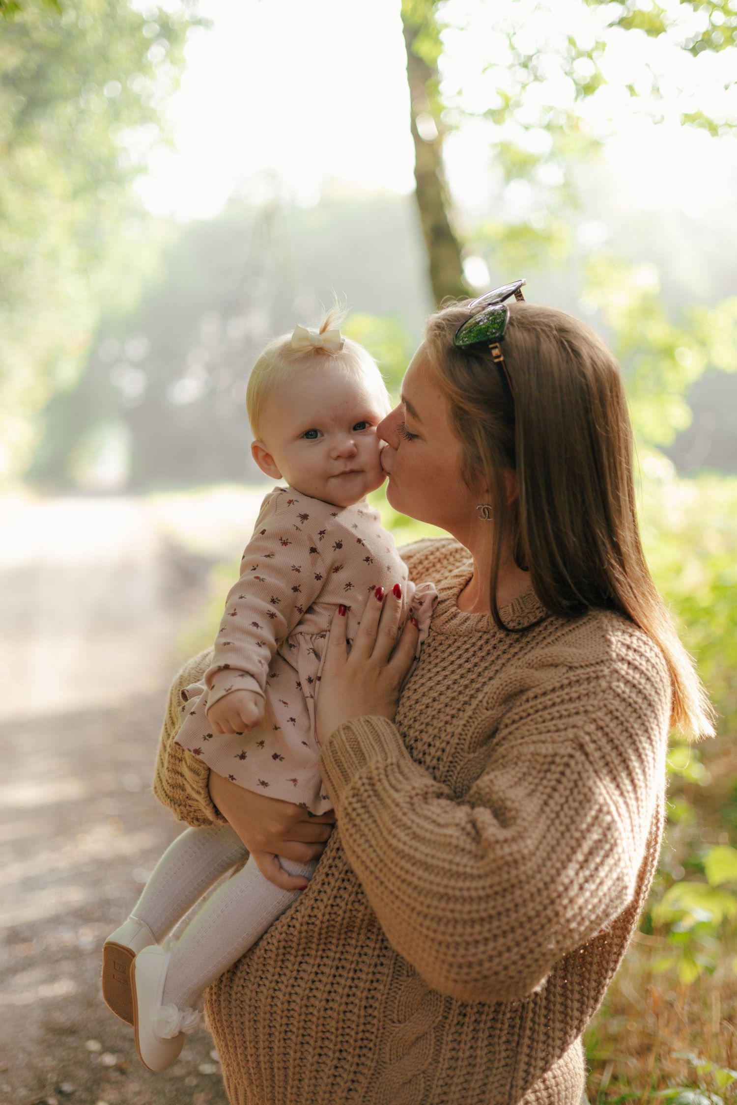 Sweet outdoor moment between person in chunky knit sweater and baby in sunlit forest.