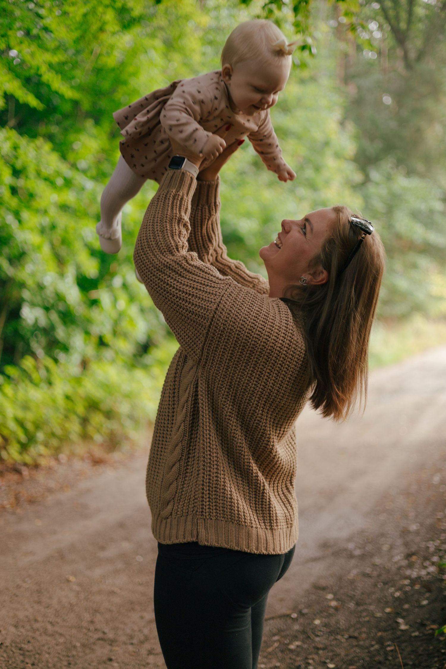 Playful moment lifting baby in air on forest path during autumn.