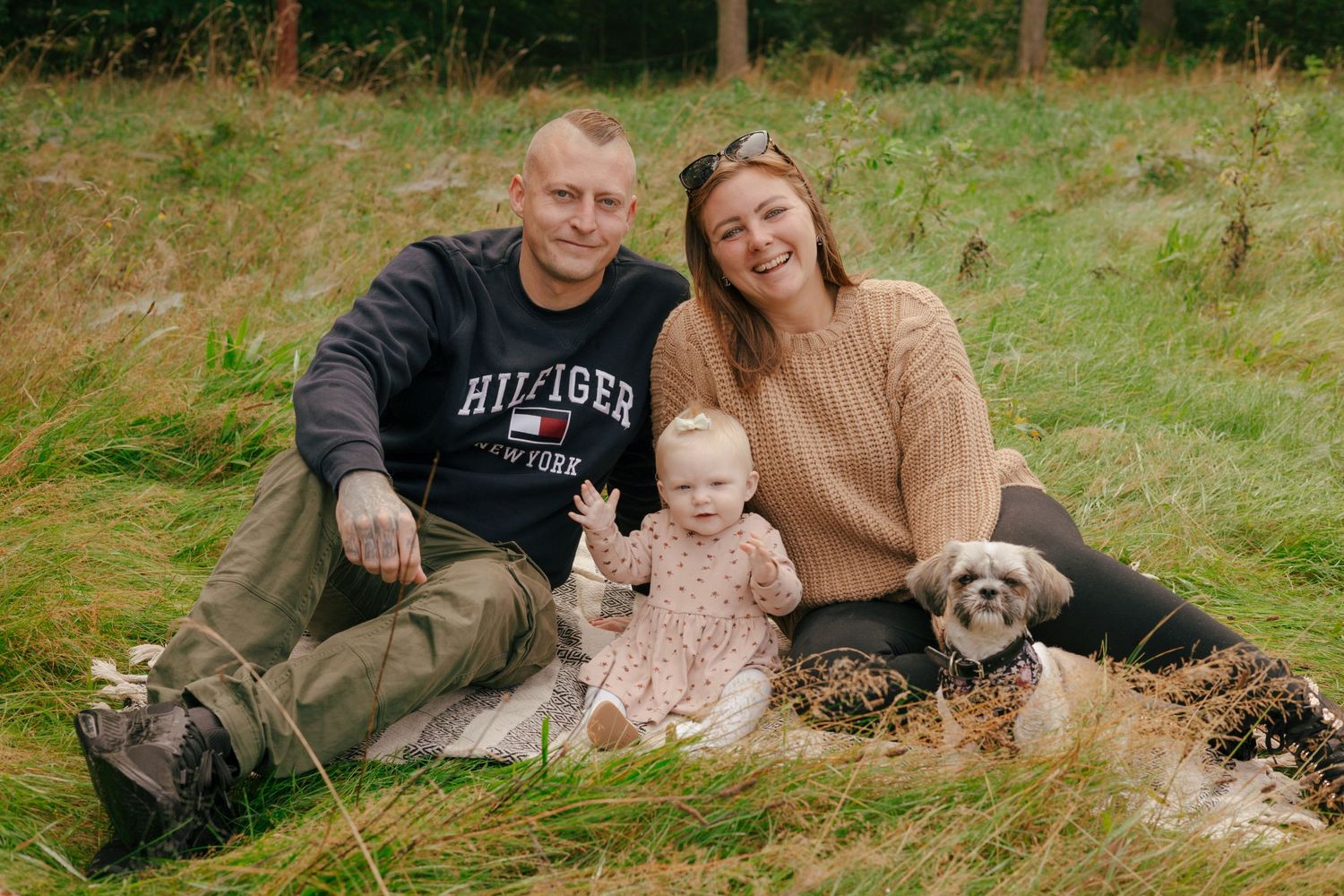 A family and their dog pose together on grass for an outdoor portrait.