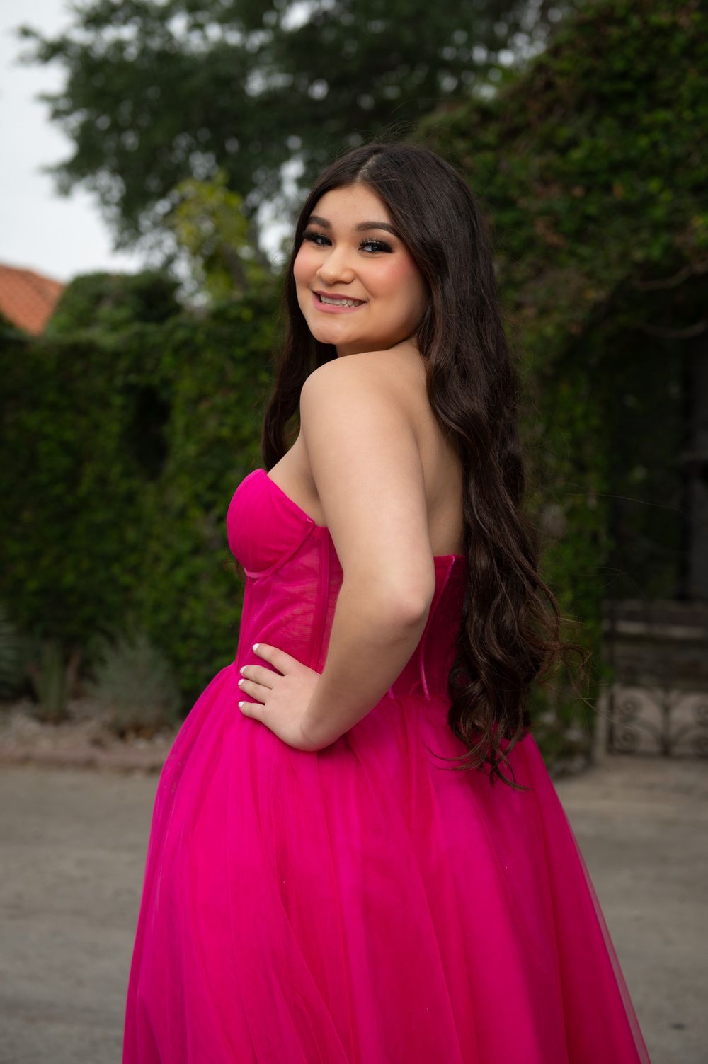 Bright fuchsia strapless ball gown photographed outdoors against greenery.