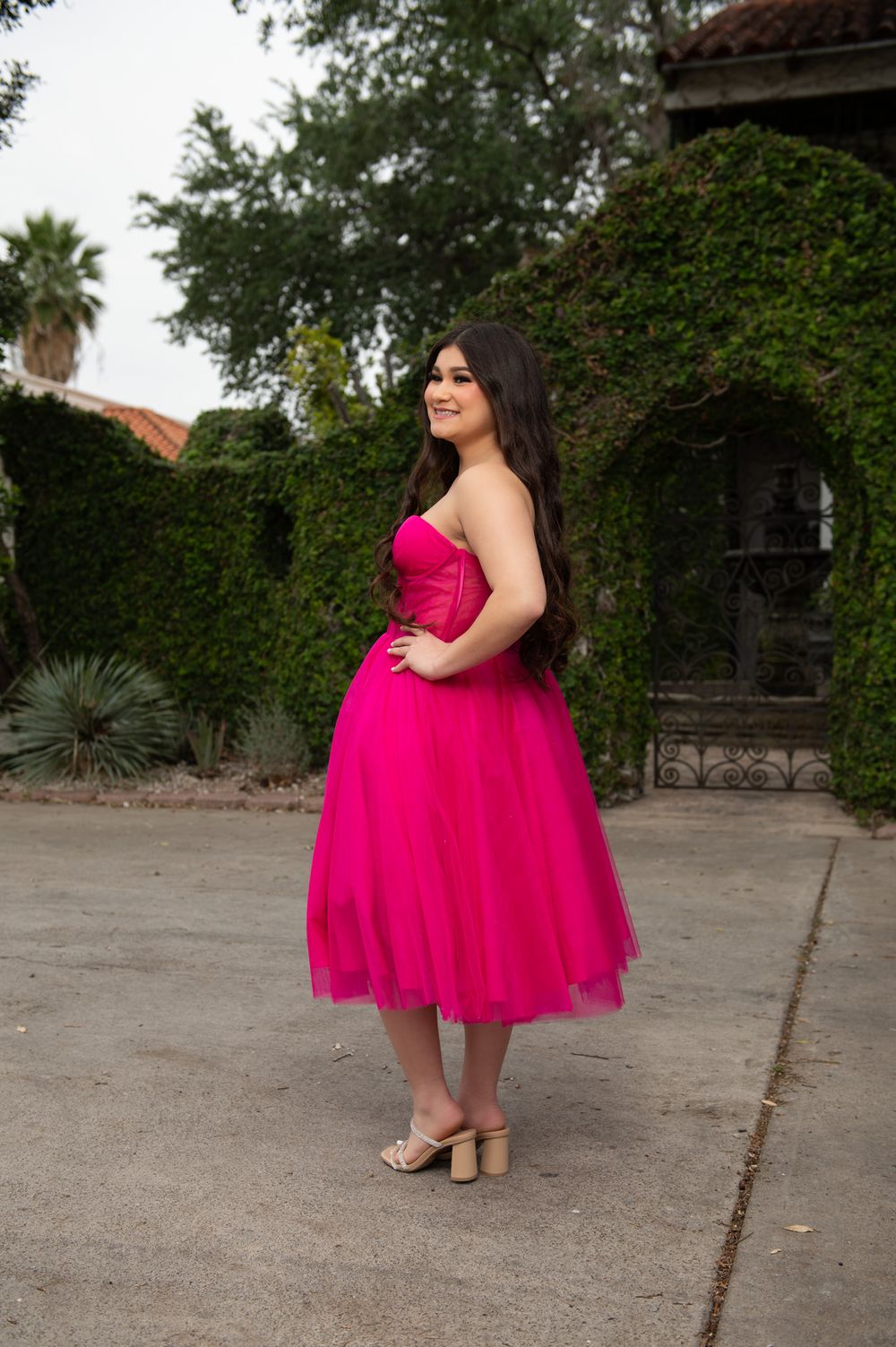 A vibrant hot pink tulle dress with a fitted bodice stands out against lush garden greenery.