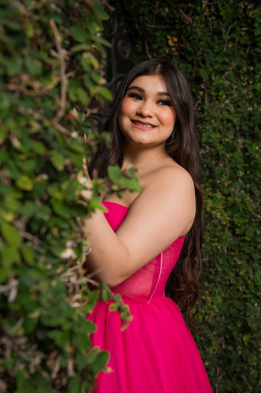 A stunning hot pink formal dress stands out beautifully against natural green foliage.
