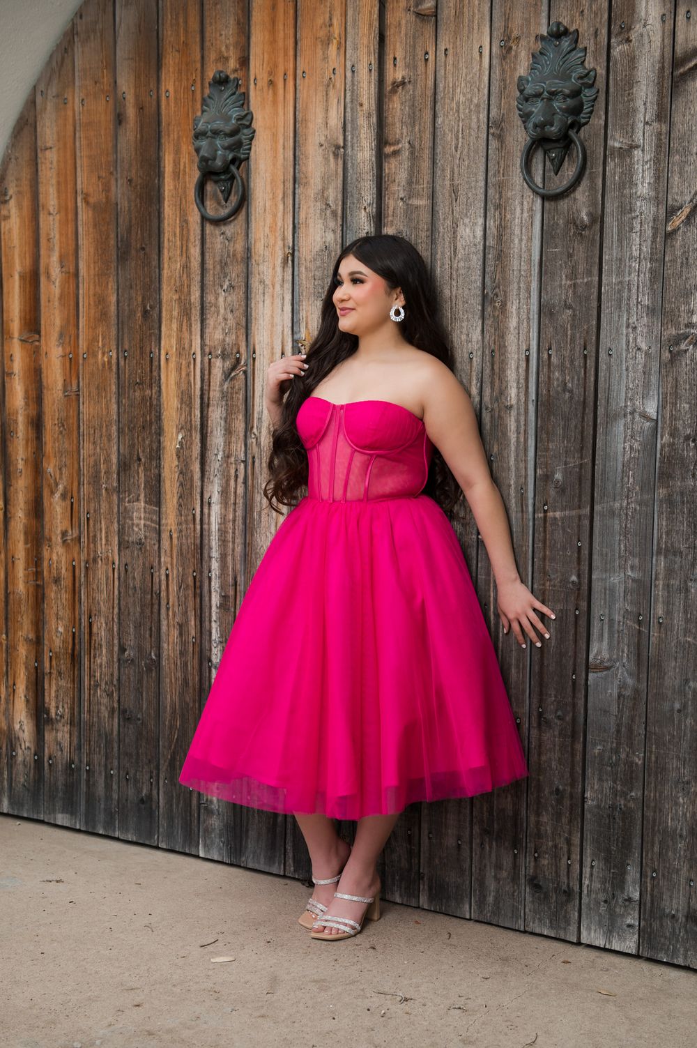 A fuchsia strapless dress with tulle skirt photographed against weathered wooden doors.