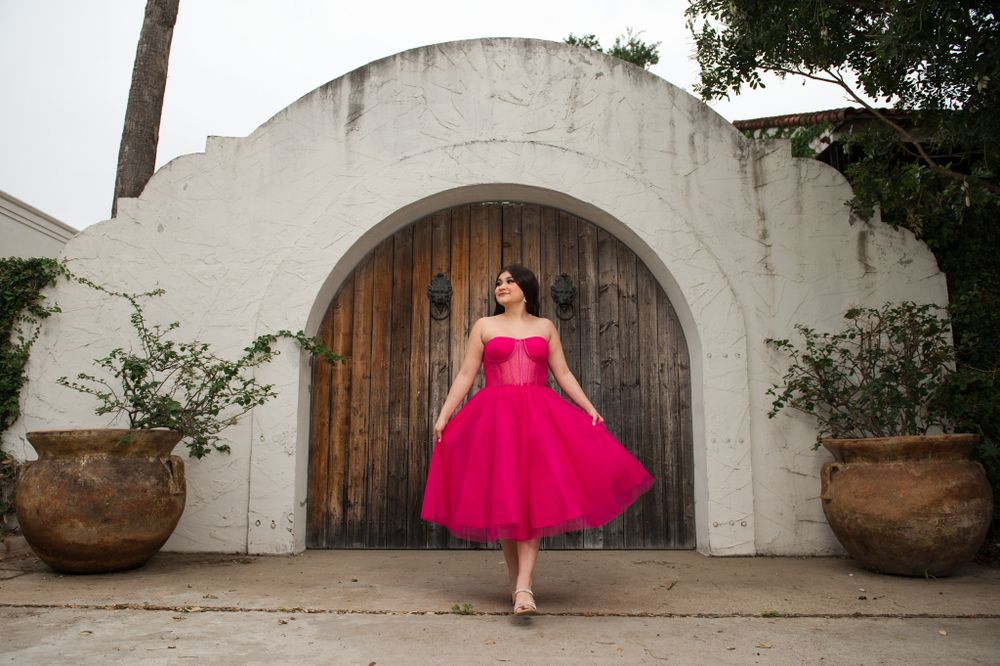 A vibrant pink formal dress photographed in front of a Spanish-style arched doorway.