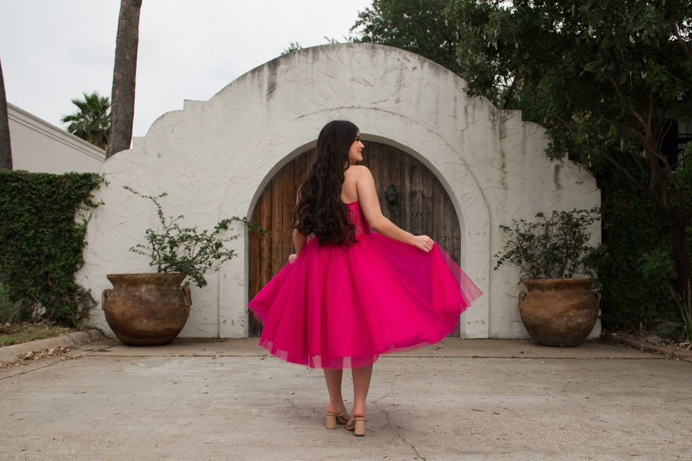 A twirling hot pink dress captured in motion against white arched architecture.