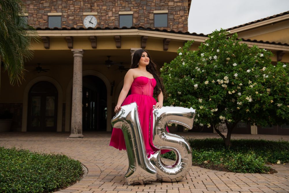 A stunning strapless magenta gown with silver number balloons decorating an elegant courtyard setting.
