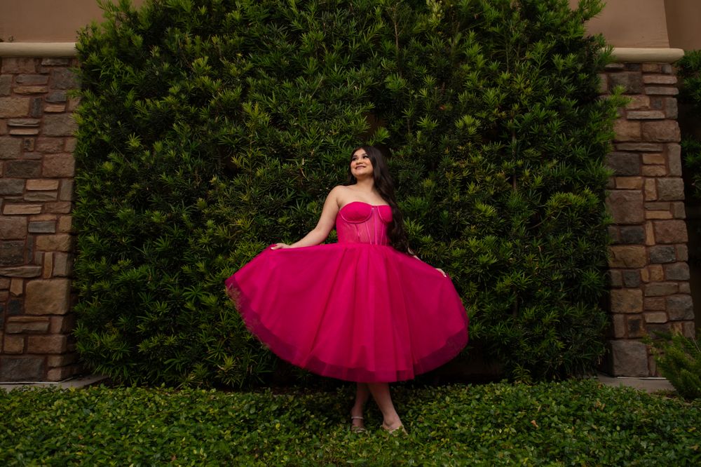 Magenta tulle dress twirls against a stone wall and green hedges in an outdoor photo shoot.