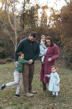 A family enjoys a tender moment together outdoors during autumn with fallen leaves and trees in the background. Durham Forest Hills Park