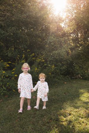 Two children in matching floral outfits sit together on a grassy hill during golden hour sunset.