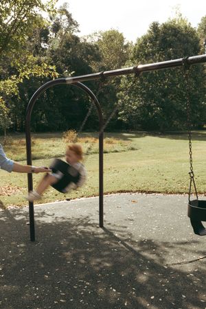 Time-lapse sequence showing someone swinging back and forth on a playground swing set in a park setting.