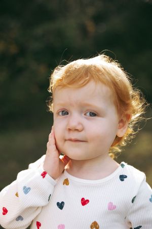 Close up of a child wearing a white sweater with colorful heart patterns.